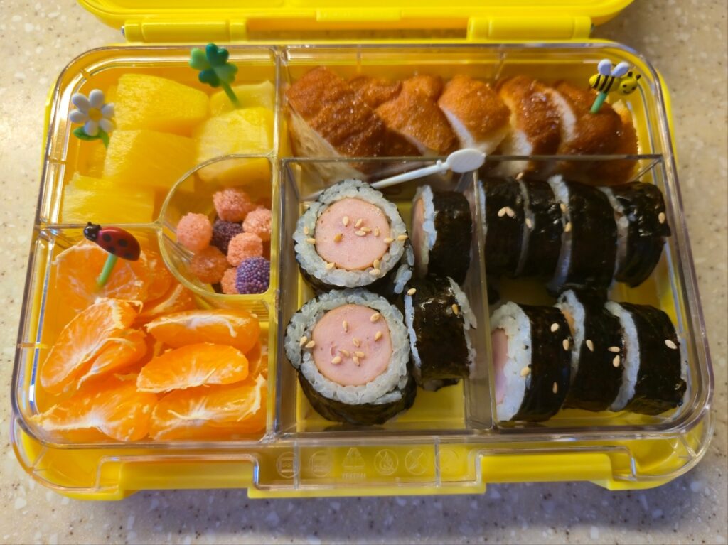 소세지 김밥, 꽈배기, 귤, 파인애플이 담긴 리틀그립 야미박스 노란색 도시락 통