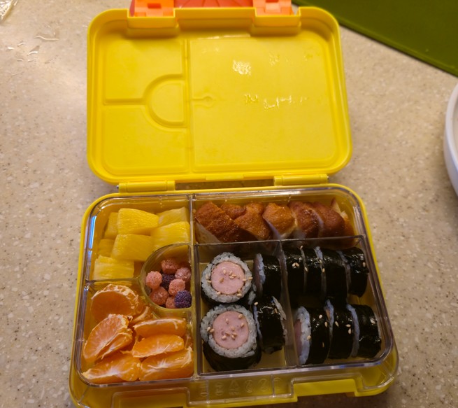 소세지 김밥, 꽈배기, 귤, 파인애플이 담긴 리틀그립 야미박스 노란색 도시락 통
